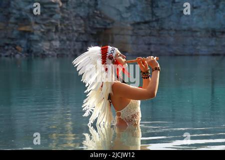 Una ragazza è vista in una cava come un indiano nativo americano. Lei è vestita tutte in bianco con un headdress bianco piume. Si vede suonare un flauto Foto Stock