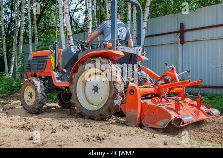 Un agricoltore su un mini trattore allenta il terreno per il prato. Coltivazione di terra, livellamento di superficie. Foto Stock