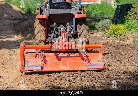 Un agricoltore su un mini trattore allenta il terreno per il prato. Coltivazione di terra, livellamento di superficie. Foto Stock