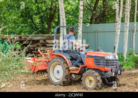 Un agricoltore su un mini trattore allenta il terreno per il prato. Coltivazione di terra, livellamento di superficie. Foto Stock