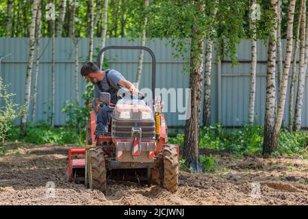 Un agricoltore su un mini trattore allenta il terreno per il prato. Coltivazione di terra, livellamento di superficie. Foto Stock