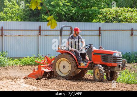 Un agricoltore su un mini trattore allenta il terreno per il prato. Coltivazione di terra, livellamento di superficie. Foto Stock