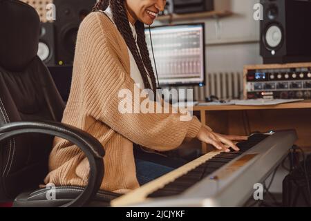 Scatto corto di giovane musicista africano femminile che suona pianoforte elettronico, sintetizzatore nel moderno studio di musica di registrazione Foto Stock