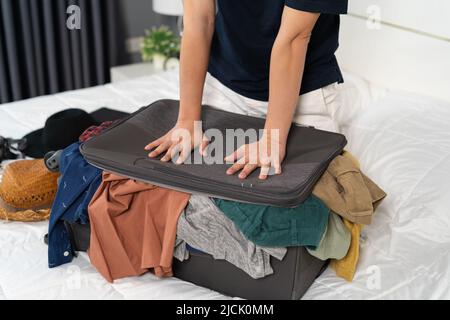 uomo che cerca di chiudere la valigia piena sul suo letto Foto Stock