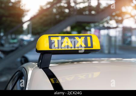 Primo piano dettaglio giallo taxi simbolo sulle auto stand sul tetto in attesa al parcheggio del terminal dell'aeroporto o stazione ferroviaria contro il parco caldo sera bokeh Foto Stock