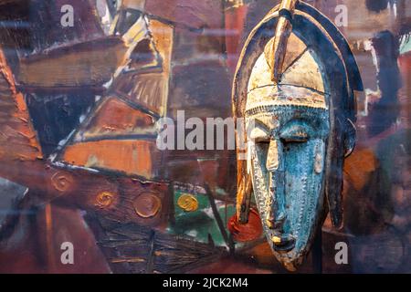 Vecchia maschera esposta nella finestra di un negozio di antiquariato. Sfondo colorato. Bruxelles. Foto Stock