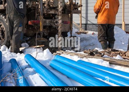 Lavoratore che utilizza tubo di metallo per pozzo artesiano. Perforazione in terra per acque sotterranee. Acqua pulita in casa Foto Stock