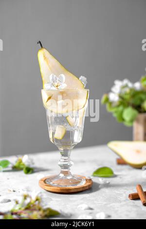 Cocktail di pere in un bicchiere decorato con frutta fresca e fiori su sfondo grigio chiaro. Estate freddo pera bere limonata con ghiaccio sul tavolo, Spark Foto Stock