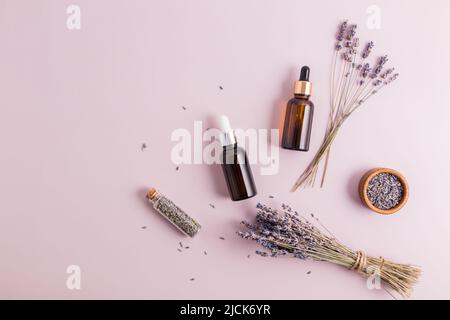 due flaconi cosmetici con pipetta con siero naturale o lavanda su sfondo viola con bouquet e semi di fiori. vista dall'alto. copia dello spazio Foto Stock