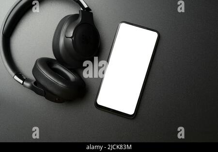 Cuffie con smartphone con schermo vuoto su sfondo nero. App per musica, ascolto di audio, podcast. Foto di alta qualità Foto Stock