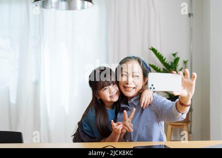 Ritratto asiatico, nonna e nipote fare attività ricreative utilizzando i loro telefoni per prendere selfie felicemente Foto Stock