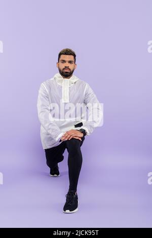 tutta la lunghezza di sportivo afro-americano con bearded in abbigliamento sportivo che fa affondo su viola Foto Stock