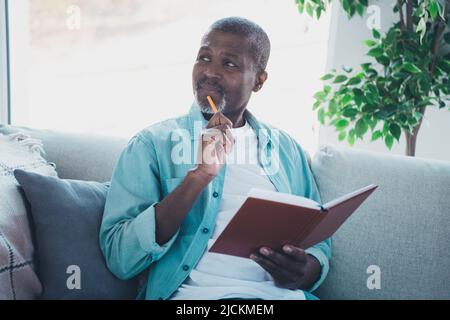 Foto di uomo anziano mentalità sedersi comodo divano hanno pensieri sulla scrittura storia notebook in soggiorno moderno Foto Stock