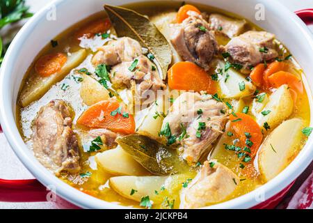 Stufato di pollo con patate e carote in pentola rossa, primo piano. Zuppa di pollo con verdure ed erbe. Ricetta per il cibo confortevole. Foto Stock