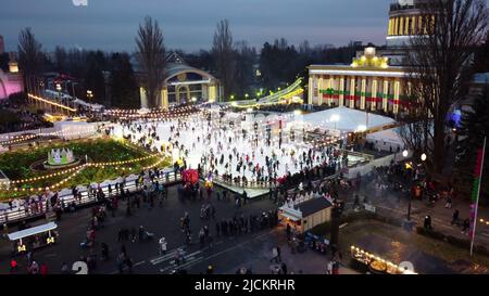 Kiev, Ucraina, 2 gennaio 2022:-bellissimo paesaggio urbano. Molte persone pattinano sulla pista di pattinaggio all'aperto con illuminazione e ghirlande la sera d'inverno nel parco pubblico della città. Drone aereo Visualizza sfondo Foto Stock