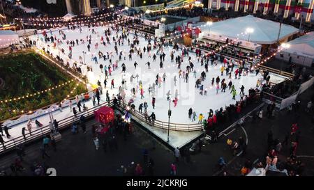 Kiev, Ucraina, 2 gennaio 2022:-bellissimo paesaggio urbano. Molte persone pattinano sulla pista di pattinaggio all'aperto con illuminazione e ghirlande la sera d'inverno nel parco pubblico della città. Drone aereo Visualizza sfondo Foto Stock