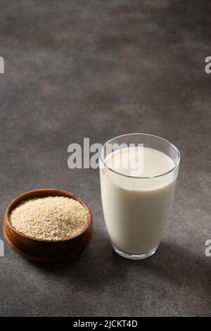 Latte di sesamo e semi di sesamo bianco in ciotola su sfondo marrone scuro. Primo piano. Vegan non latticini alternativa pianta a base di latte sostituto. Verticale. Foto Stock