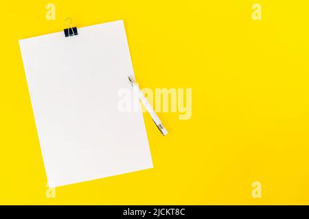 Un foglio vuoto di carta bianca per ufficio è fissato con una graffetta e una penna su uno sfondo giallo. Mockup, vuoto per l'annuncio della scheda. Foto Stock