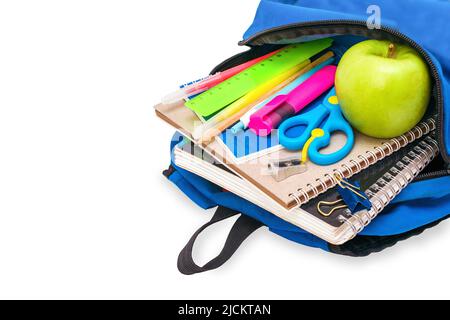 La borsa scolastica blu aperta degli studenti è piena di taccuini, penne, pennarelli, cancelleria e una mela verde si trova sul suo lato, isolato su sfondo bianco. Foto Stock