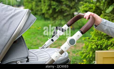 La madre scogli passeggino con il bambino seduto su panca nel parco Foto Stock