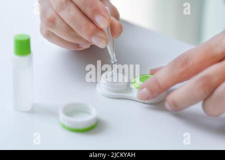 Come mettere le lenti a contatto: Passo per passo istruzioni foto. Passo 1: Ragazza rimuovere la lente dal contenitore con pinzette di aiuto. Primo piano di mani e lenti. Foto Stock
