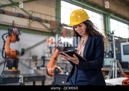 Ingegnere di automazione femminile con tablet per la programmazione del braccio robotico in fabbrica. Foto Stock