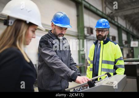 Manager supervisori e lavoratori industriali in uniforme fare il controllo in grande fabbrica di metallo e parlare. Foto Stock