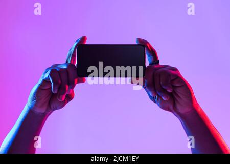 Immagine dello schermo dello smartphone. Primo piano di un giovane uomo nero con dispositivo mobile vuoto, consigliando una nuova app in neon light Foto Stock