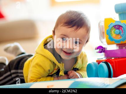 Un bambino di pochi mesi suona sorridendo su un tappeto morbido insieme ai suoi giocattoli. Foto Stock