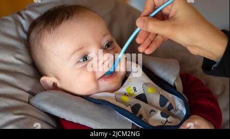 Primo piano di un bambino di pochi mesi che inizia lo svezzamento mangiando una purea di frutta. Foto Stock