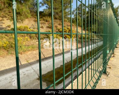 Recinzione in filo di acciaio verde con aste vicino al canale di irrigazione Foto Stock