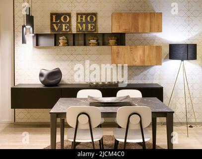 Tavolo da pranzo con sedie situato contro mensole con decorazioni nel moderno soggiorno di casa Foto Stock