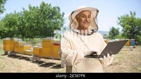 Apicoltore in uniforme che lavora su un computer portatile su apiario Foto Stock