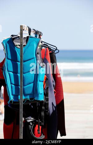 Una fila di mute appese su una rastrelliera di una scuola di surf. Immagine ritratto Foto Stock