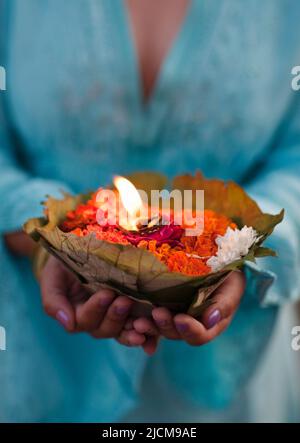 Una donna fa un'offerta floreale al fiume Ganges al tramonto a Rishikesh, Uttarakhand, India. Foto Stock