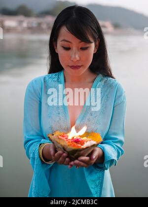 Una donna fa un'offerta floreale al fiume Ganges al tramonto a Rishikesh, Uttarakhand, India. Foto Stock