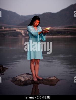 Una donna fa un'offerta floreale al fiume Ganges al tramonto a Rishikesh, Uttarakhand, India. Foto Stock