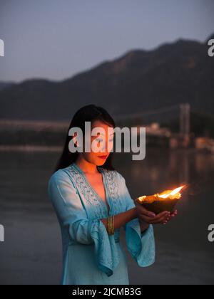 Una donna fa un'offerta floreale al fiume Ganges al tramonto a Rishikesh, Uttarakhand, India. Foto Stock