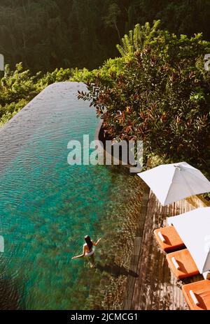 Donna che guadi nella piscina a sfioro principale, i Giardini di Hanging di Ubud, Bali, Indonesia. La piscina a sfioro principale si affaccia sulla valle del fiume Ayung. Foto Stock