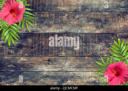 Fiori di Hibiscus e foglie di palma tropicali su sfondo rustico in legno Foto Stock