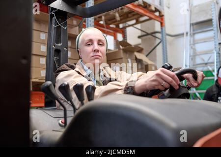 Ritratto di giovane donna in abiti da lavoro che guida il caricatore sul magazzino logistica Foto Stock