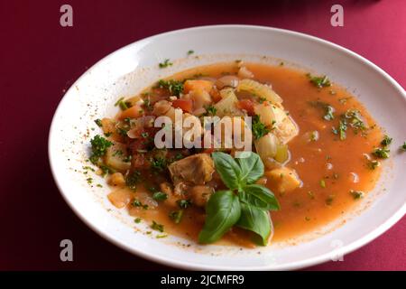 Gustosa Bouillabaisse, frutti di mare e zuppa di pesce, servita su un piatto bianco, con decorazioni basilico Foto Stock