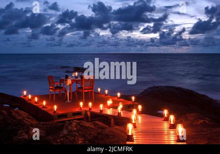 Un cameriere accende le candele e fissa un tavolo per due per una cena romantica sulla spiaggia. Aturuwella, Bentota, Sri Lanka. Foto Stock