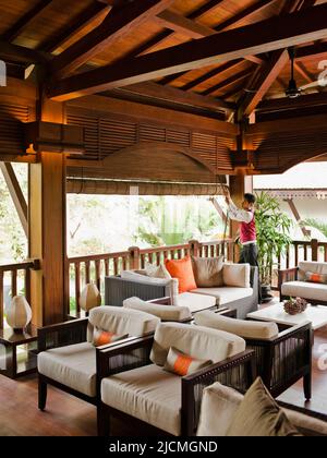 Un membro del personale dell'hotel attira le tende del salotto al secondo piano per lasciare la luce del mattino al la Residence d'Angkor, Siem Reap, Cambogia. Foto Stock