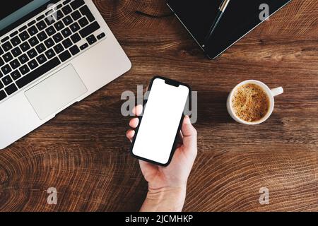 Freelance che utilizza il telefono cellulare con schermo bianco bianco bianco bianco bianco mockup alla scrivania dell'ufficio, vista dall'alto Foto Stock
