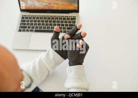 L'uomo che ha artrite reumatoide indossa guanti di compressione per alleviare il dolore nelle sue mani Foto Stock