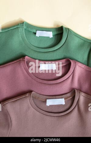 Bianco bianco bianco etichetta etichetta etichetta mockup su tre nuovo abito verde, rosa polveroso e beige cotone camicie tessuto tessuto tessuto sfondo. Collare rotondo longsleev Foto Stock