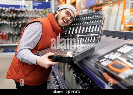 uomo soddisfatto che tiene il set di bussole e teste di chiave nel negozio di ferramenta Foto Stock