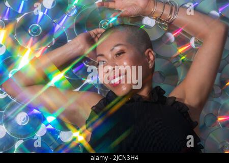 Divertimento e musica concetto. Ritratto di bella e felice con sorriso Thai donna sdraiata su compact disc sfondo. Modello illuminato con lucida e. Foto Stock