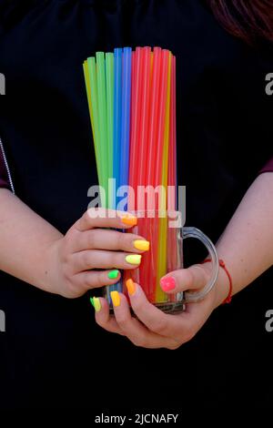 donna con le estensioni delle unghie dipinte in una varietà di colori che tiene il vetro riempito con cannucce colorate di plastica potabile Foto Stock